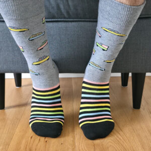 Primer plano de una persona vistiendo calcetines navideños de color verde con estampado de sellos postales festivos, regalos y matasellos "Happy Holidays".