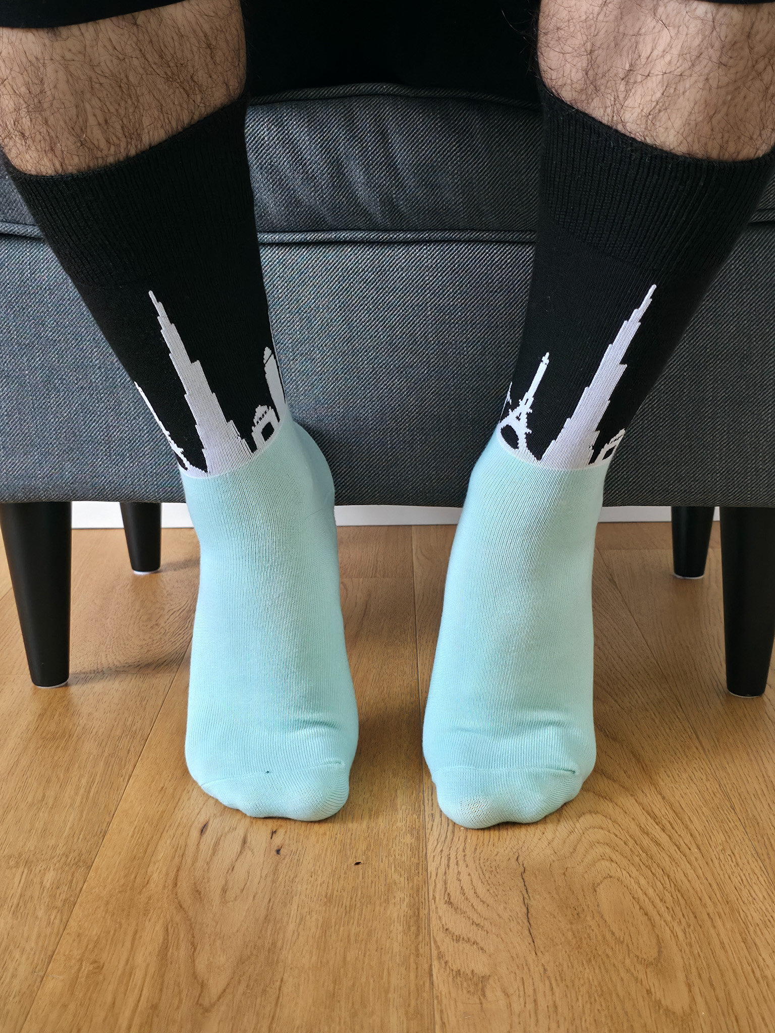 Primer plano de una persona vistiendo calcetines de caña alta bicolor, con fondo negro y siluetas blancas de monumentos del mundo como la Torre Eiffel, y pie en tono verde agua.
