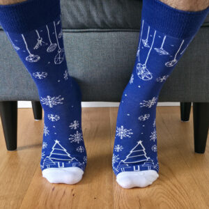 Primer plano de una persona vistiendo calcetines navideños de color azul rey con estampado blanco de copos de nieve, esferas colgantes y árboles de Navidad.