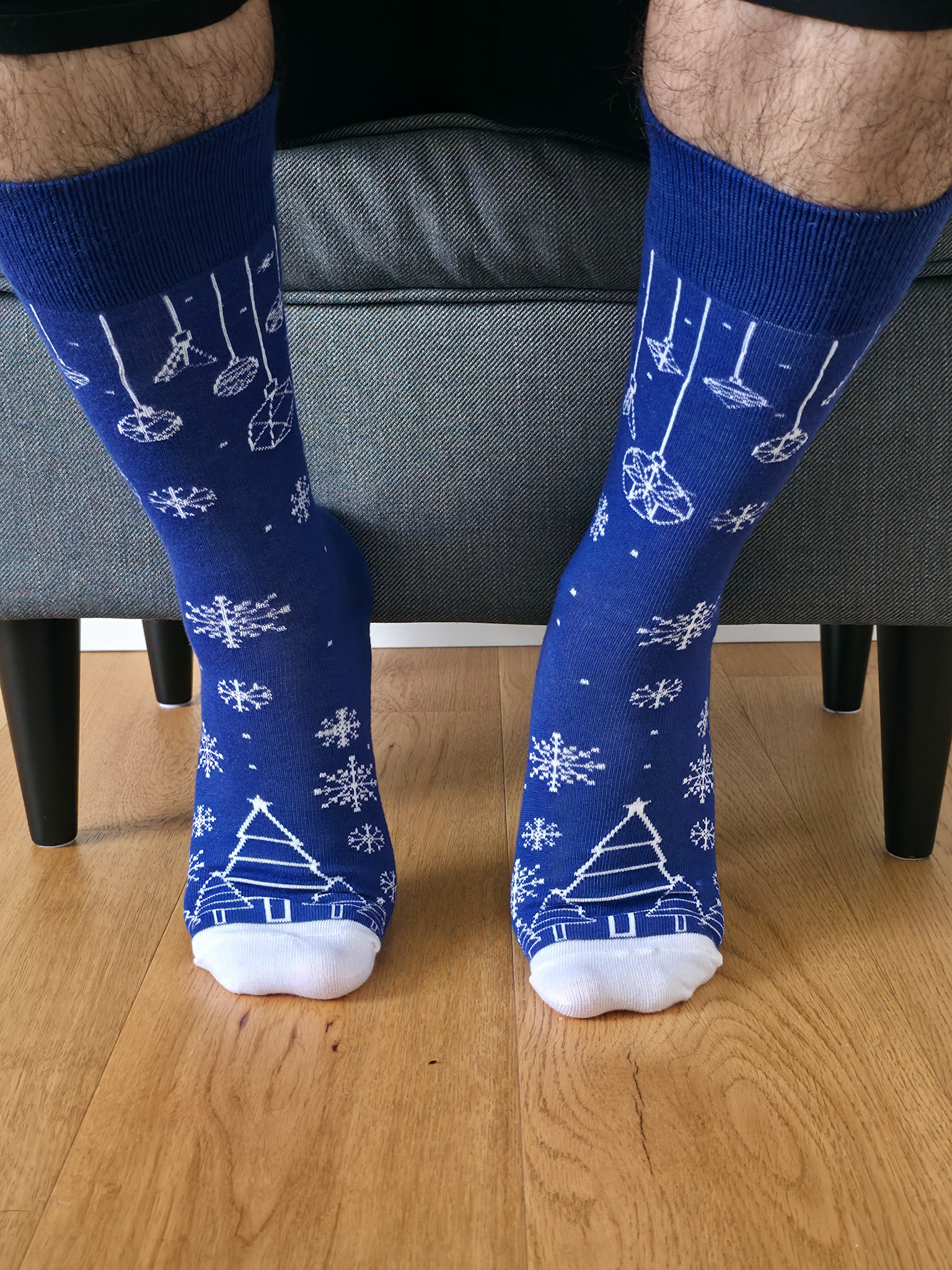 Primer plano de una persona vistiendo calcetines navideños de color azul rey con estampado blanco de copos de nieve, esferas colgantes y árboles de Navidad.