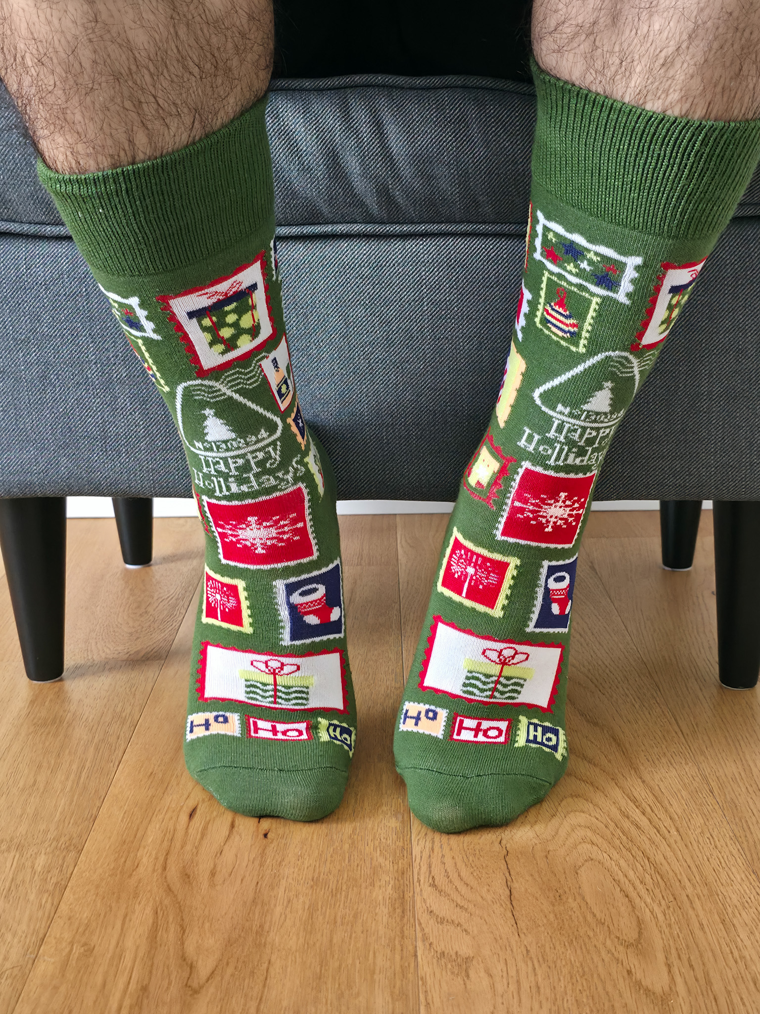 Primer plano de una persona vistiendo calcetines navideños de color verde con estampado de sellos postales festivos, regalos y matasellos "Happy Holidays".