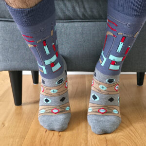 Primer plano de una persona usando calcetines grises con estampado de herramientas de bricolaje, incluyendo martillos, alicates, tuercas y tornillos.