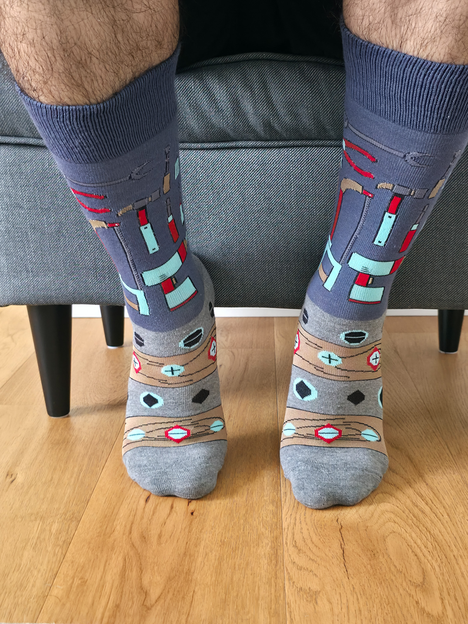 Primer plano de una persona usando calcetines grises con estampado de herramientas de bricolaje, incluyendo martillos, alicates, tuercas y tornillos.