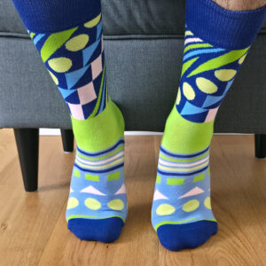 Primer plano de una persona vistiendo calcetines divertidos con estampado geométrico abstracto en tonos azul eléctrico, verde lima, celeste y rosa pastel.
