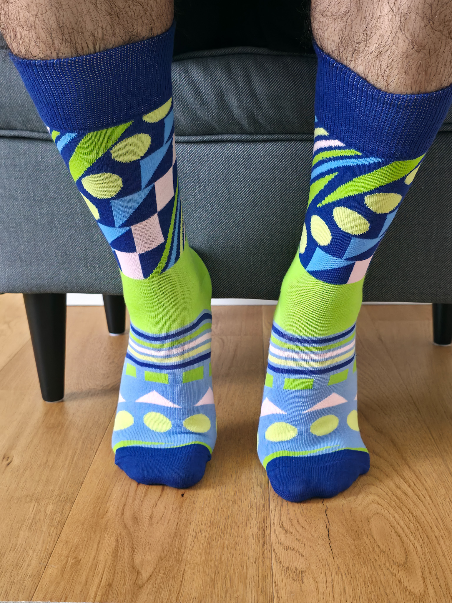 Primer plano de una persona vistiendo calcetines divertidos con estampado geométrico abstracto en tonos azul eléctrico, verde lima, celeste y rosa pastel.